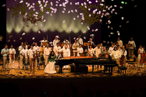 Grupo de pessoas num palco com instrumentos musicais e microfone em cima de mesa